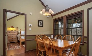A dining room with a wooden table and chairs, a chandelier, and a window with a view of trees.