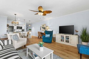 A modern living room with a sofa, a coffee table, a TV, and a ceiling fan. - Beach Front w/ Beautiful Sunsets! Walk to Pools! Amenity Access included! Dog Friendly! (Seabrook Island)