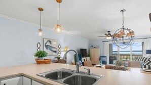 A kitchen with a double sink, pendant lights, and a view of the ocean.
