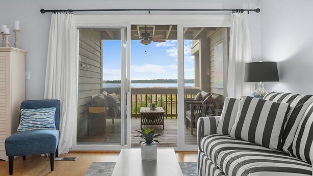 A living room with a sofa, a chair, a coffee table, and a view through a sliding glass door to an outdoor deck.