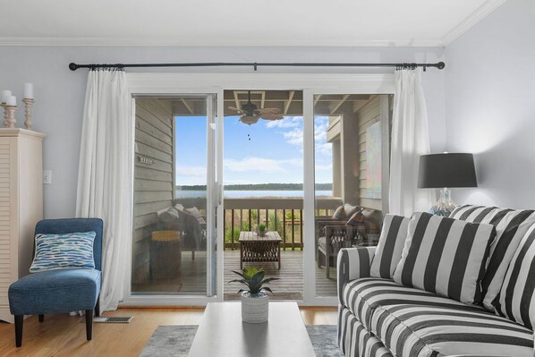 A living room with a sofa, a chair, a coffee table, and a view through a sliding glass door to an outdoor deck.