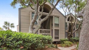 A two-story building with a porch, surrounded by trees and shrubs.