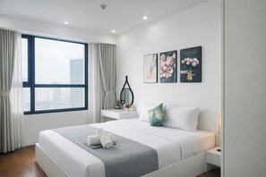 A modern hotel room with a large bed, a desk, and a view of the city.