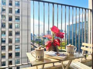 A balcony with a table, two mugs, a book, and a potted plant.