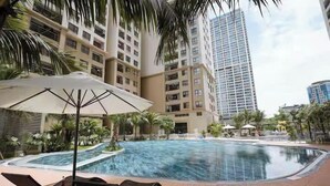 A swimming pool area with lounge chairs and umbrellas, surrounded by tall residential buildings.