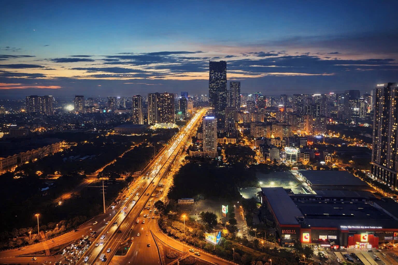 A cityscape at night with high-rise buildings, a highway, and a large commercial building with signage.