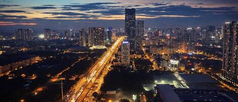 A cityscape at night with high-rise buildings, a highway, and a large commercial building with signage.