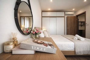 A modern bedroom with a large bed, a bedside table with a magazine, a mirror, and a vase with flowers.