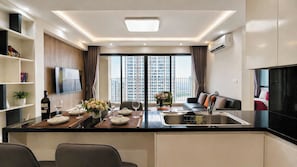 A modern kitchen with a dining area, a flat-screen TV, and a view of high-rise buildings.