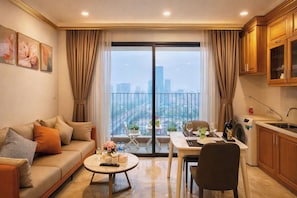 A modern living room with a sofa, coffee table, and dining area, a balcony with a city view, and a kitchen with wooden cabinets.