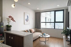 A modern living room with a sofa, a coffee table, a potted orchid, and a city view through large windows.