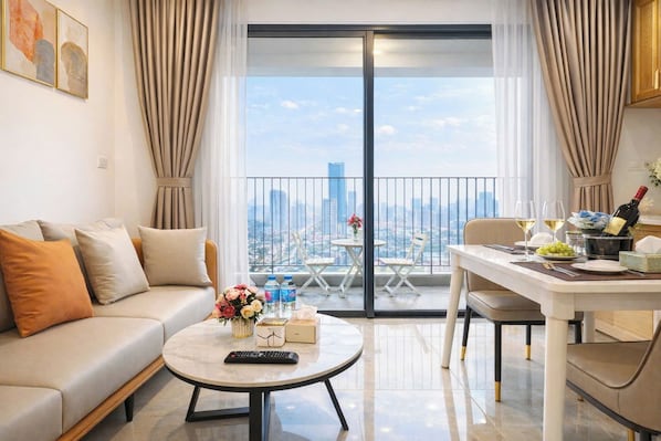 A modern living room with a sofa, coffee table, and dining area with a view of the cityscape.