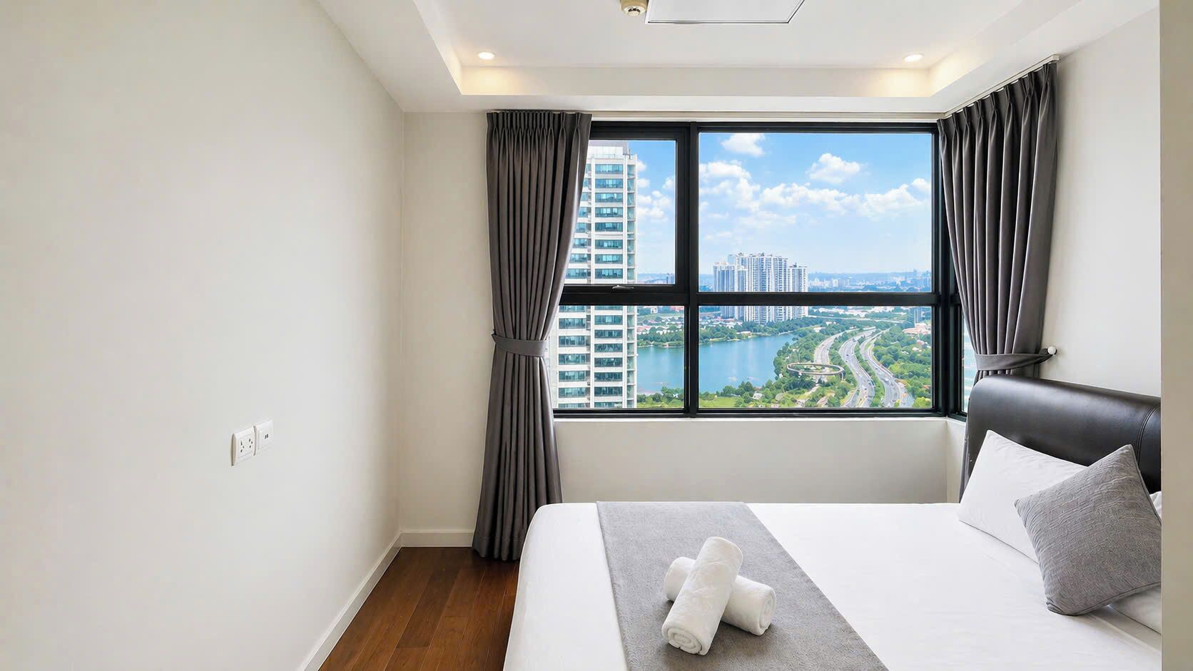 A hotel room with a large window, a bed, a headboard, and a view of a cityscape.