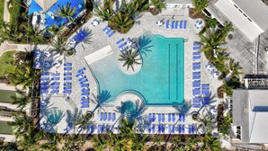 Vue aérienne d’un complexe hôtelier doté d’une piscine centrale, entourée de transats et de palmiers.