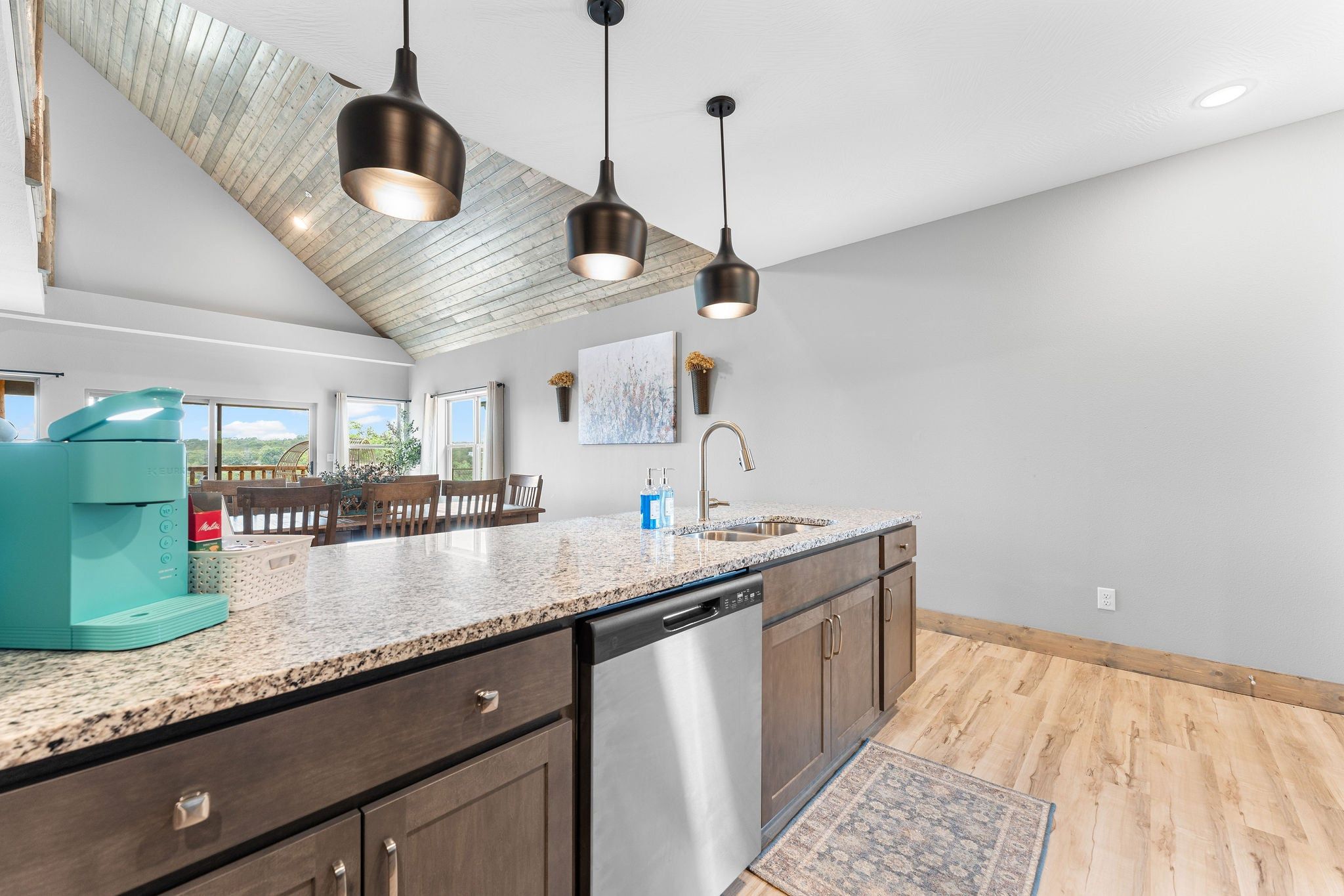A modern kitchen with a granite countertop, stainless steel dishwasher, and dark wooden cabinets.