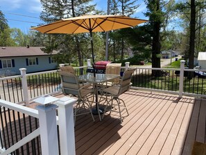 Une terrasse avec une table et des chaises en verre, un barbecue et un parasol.