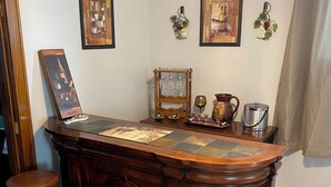 Una zona de bar con mostrador de madera, cuatro taburetes, un letrero de degustación de vinos y cuadros enmarcados en las paredes.