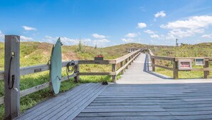 Un muelle de madera que conduce a una playa, con una tabla de surf y un letrero que prohíbe el acceso a carritos más allá de un punto determinado.