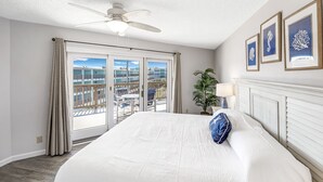 A hotel room with a large bed, a ceiling fan, a balcony with a view of the city, and framed artwork on the wall. - La Mirage Condo 316LK Beachfront Resort Condominiums with Private Boardwalk (Port Aransas)