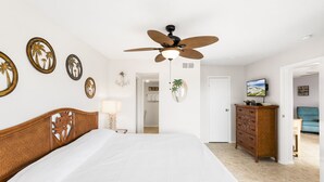 A hotel room with a large bed, a ceiling fan, a dresser, and a television.