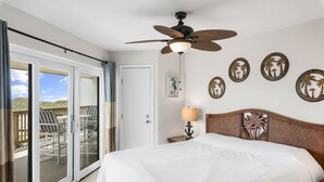 A bedroom with a bed, a ceiling fan, a nightstand with a lamp, and a view of a balcony with chairs. - La Mirage Condo 211L- Beach Condominium Resort with Private Boardwalk to BEACH (Port Aransas)