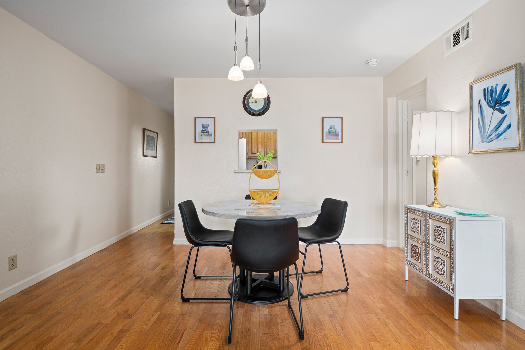 A dining area with a round table, black chairs, a white cabinet, and a hanging light fixture.