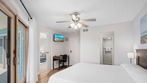 Ein Hotelzimmer mit einem großen Bett, einem Schreibtisch mit Stuhl, einem Deckenventilator, einem Fernseher und einer Badezimmertür.