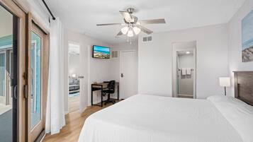 Ein Hotelzimmer mit einem großen Bett, einem Schreibtisch mit Stuhl, einem Deckenventilator, einem Fernseher und einer Badezimmertür.