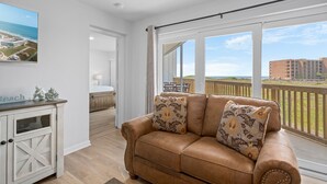 Ein großzügiger Wohnbereich mit Ledersofa, Esstisch und einem Balkon mit Blick auf Strand und Gebäude.