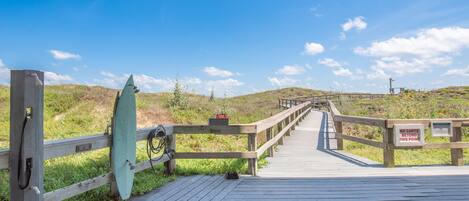 A wooden boardwalk leading to a beach with a surfboard and a sign prohibiting carts beyond a certain point.