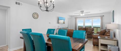 A dining area with a wooden table and teal chairs, a chandelier, and a view of the outdoors.