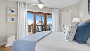 A bedroom with a bed, a ceiling fan, a nightstand, a lamp, and a view of a building outside.