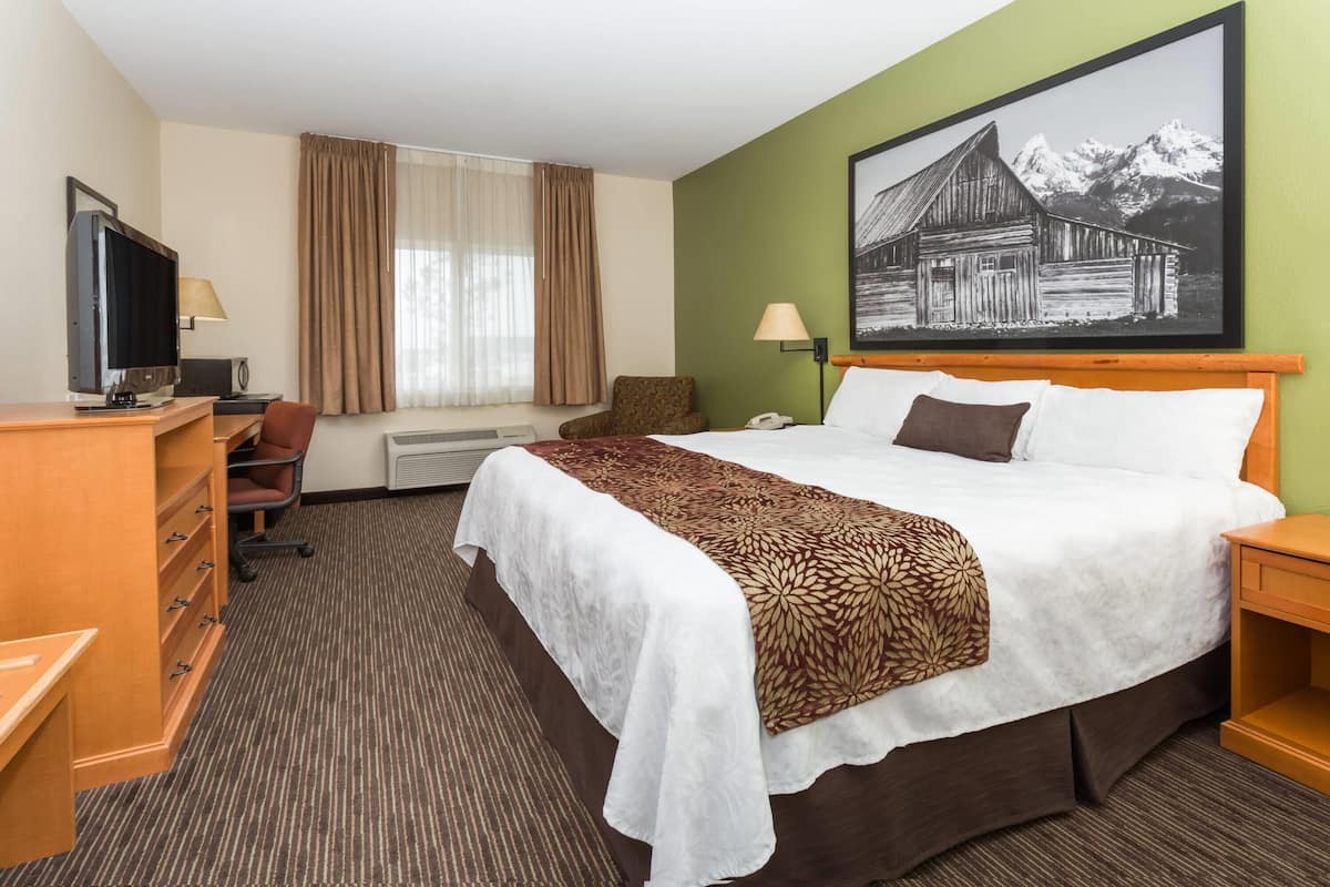 Ein Hotelzimmer mit Bett, Schreibtisch, Stuhl, Fernseher und einem großen Gemälde an der Wand.