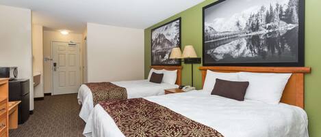 A hotel room with two beds, a desk, a lamp, and a framed picture on the wall.