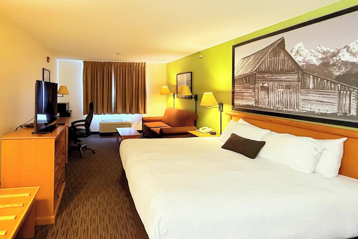 Ein Hotelzimmer mit einem großen Bett, einem Schreibtisch mit Computer, einem Sessel und einem Fernseher.