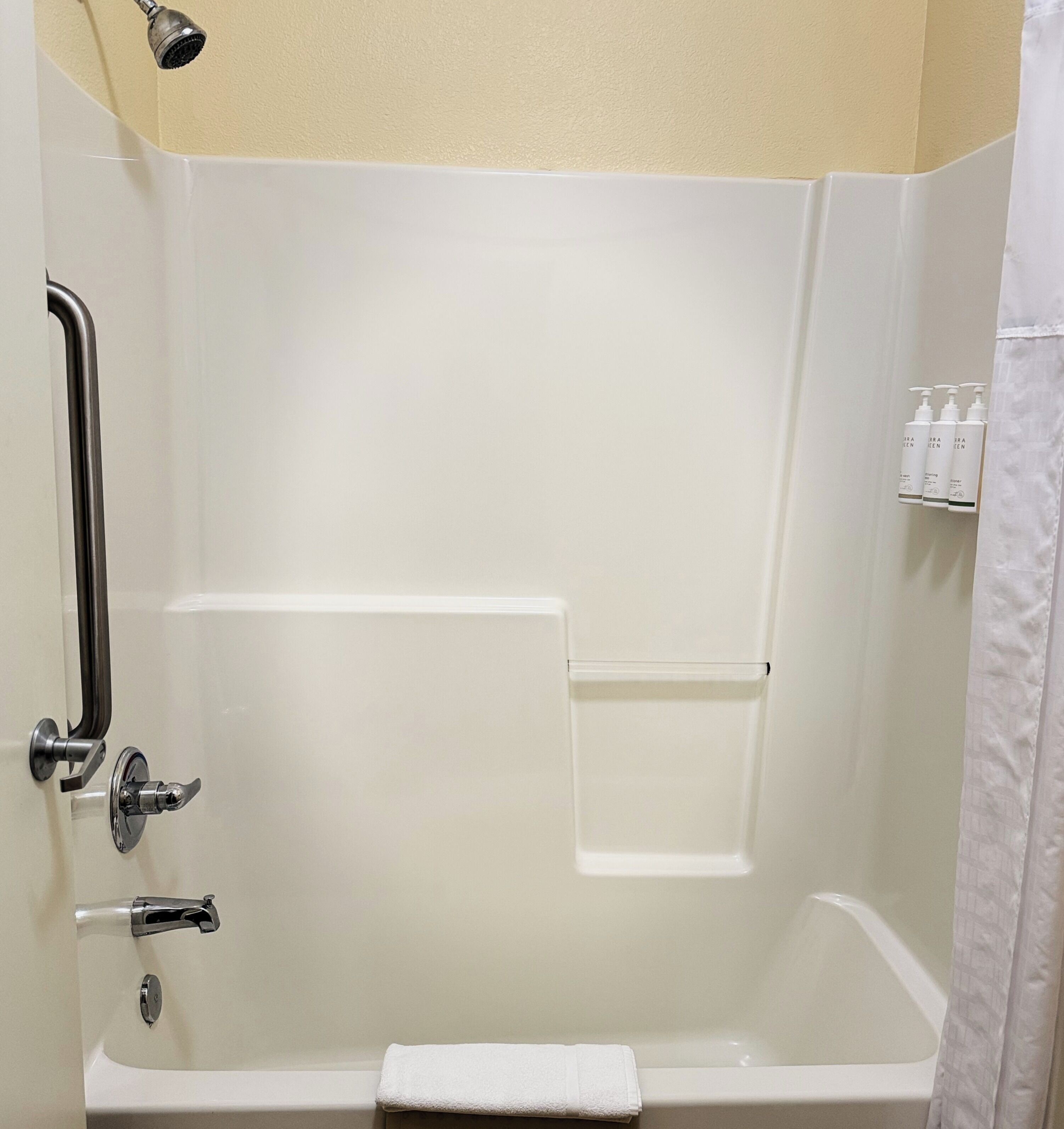 A white bathtub with a showerhead, a towel, and a shelf with toiletries.