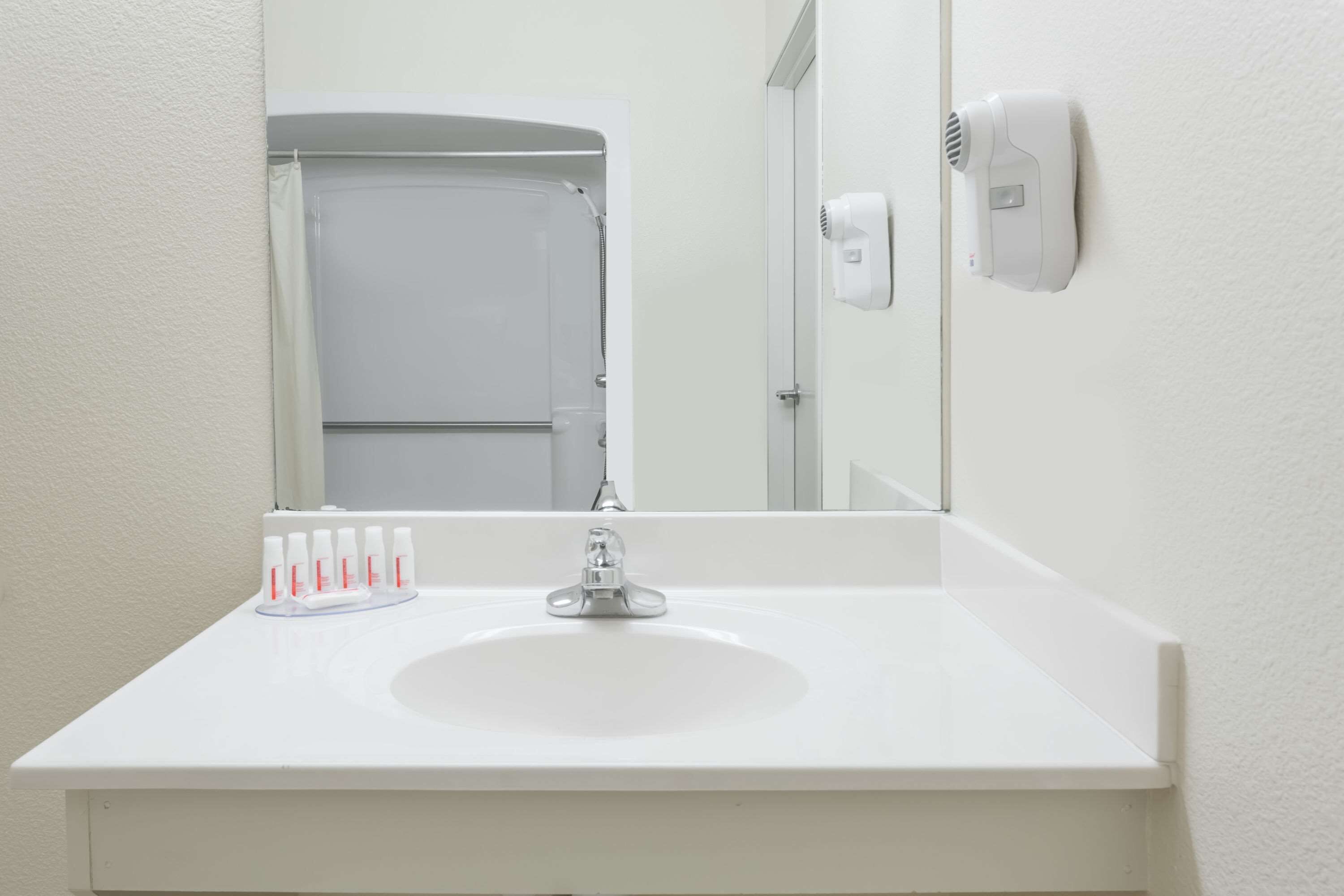 A bathroom with a white sink, a mirror, and a hair dryer mounted on the wall.