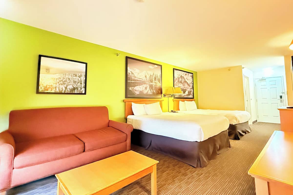 Ein Hotelzimmer mit einem roten Sofa, einem Bett mit zwei Kissen, einem Nachttisch und zwei gerahmten Bildern an der Wand.
