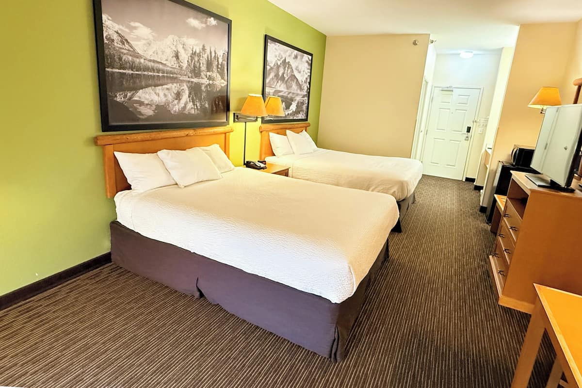 Ein Hotelzimmer mit zwei Betten, einem Schreibtisch, einem Stuhl, einem Fernseher und zwei gerahmten Bildern an der Wand.