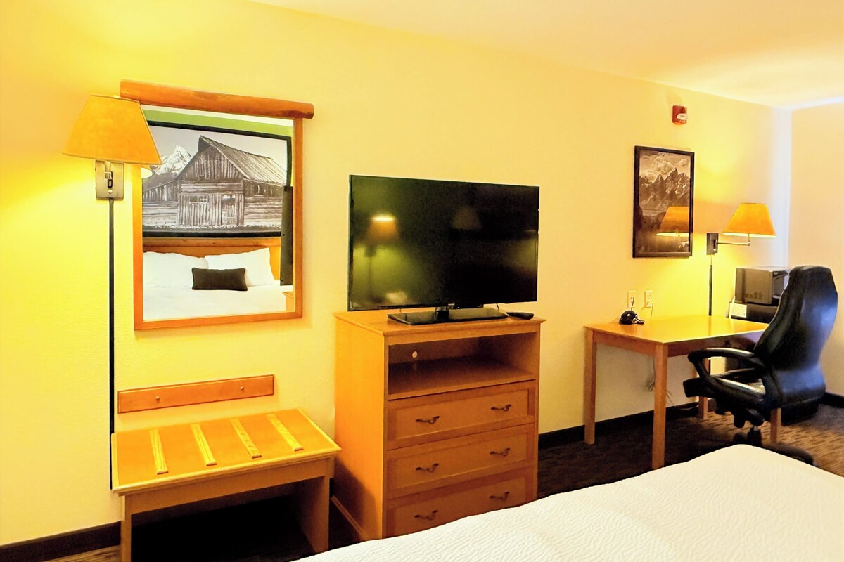 A hotel room with a bed, a desk with a computer, a television, a chair, and two lamps.
