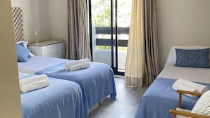 Habitación de hotel con dos camas, una mesita, una silla y un amplio ventanal corredero que da a un espacio al aire libre.