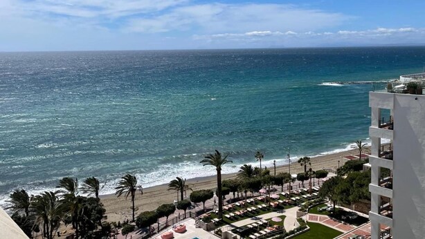 A beachfront hotel with a pool area, palm trees, and ocean views.