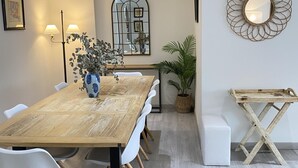 A modern dining area with a wooden table, white chairs, a vase with dried flowers, a potted plant, and a decorative mirror on the wall.