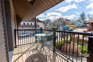 A balcony with a wooden floor, metal railing, and two green chairs. - Charming Downtown Two Bedroom w/ Fireplace (New Glarus)