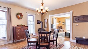 A dining area with a wooden table and chairs, a chandelier, and a rug. - Charming Downtown Two Bedroom w/ Fireplace (New Glarus)