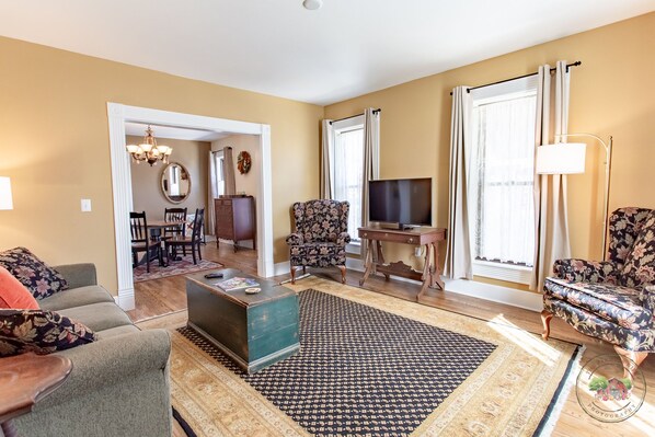A living room with a sofa, armchair, TV, and a patterned rug. - Charming Downtown Two Bedroom w/ Fireplace (New Glarus)