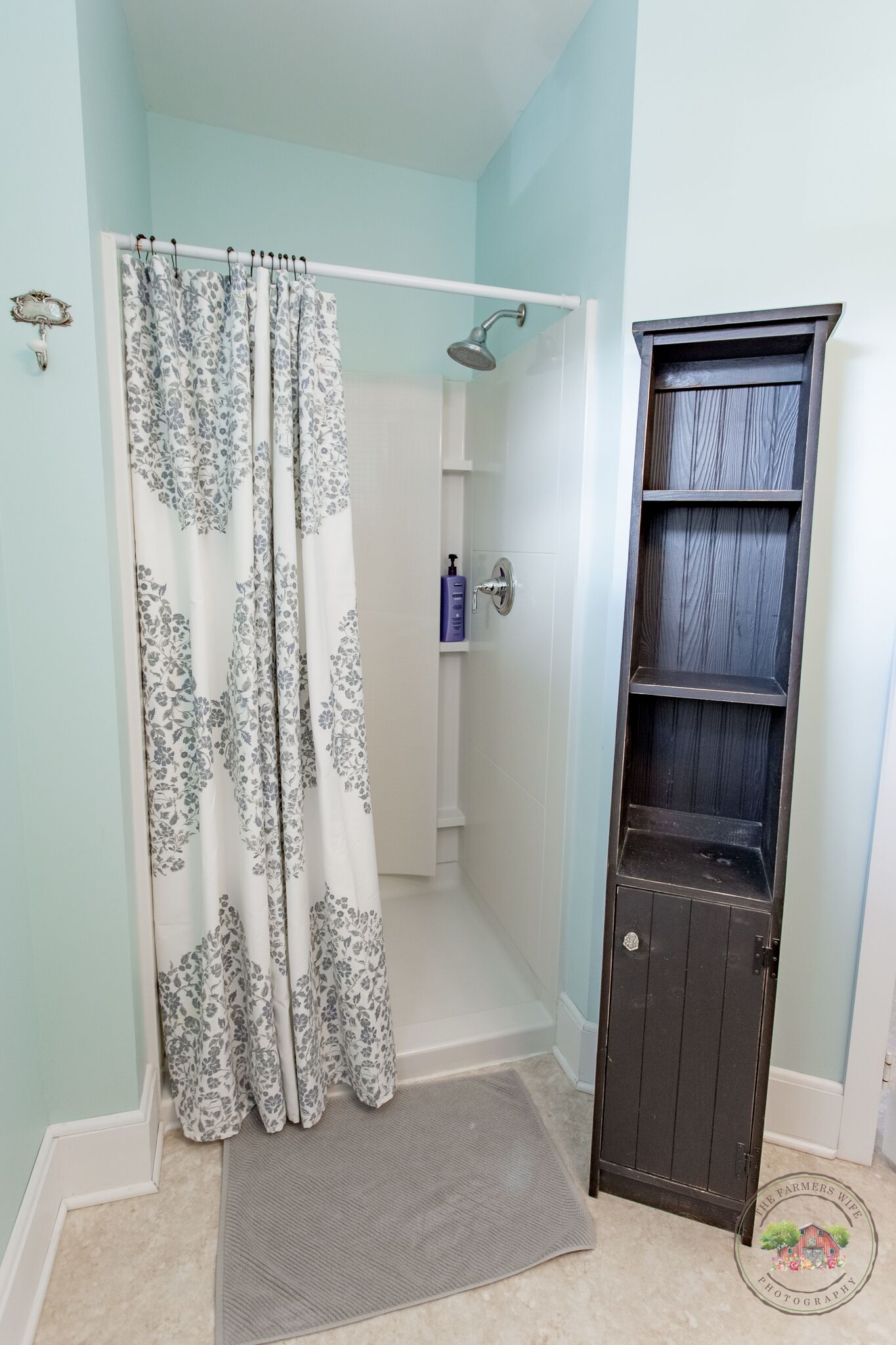 A bathroom with a shower, a dark wooden cabinet, and a floral shower curtain.