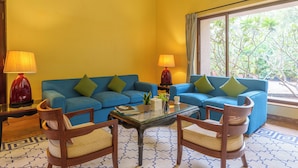 A living room with two blue sofas, a glass coffee table, wooden chairs, and lamps. - Amã Stays & Trails Kihim Courtyard, Alibag (Alibag)