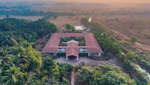 A large building with a red roof, surrounded by lush greenery and palm trees. - Amã Stays & Trails Kihim Courtyard, Alibag (Alibag)