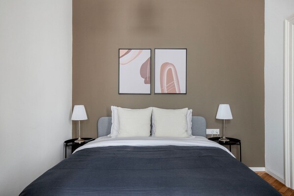 Une chambre à coucher comprenant un lit, deux tables de chevet avec des lampes et deux œuvres d’art abstraites accrochées au mur.